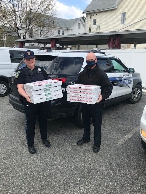 Two police officers are holding boxes of pizza in front of a police car.