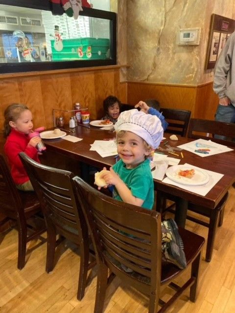A little boy wearing a chef hat sits at a table with other children