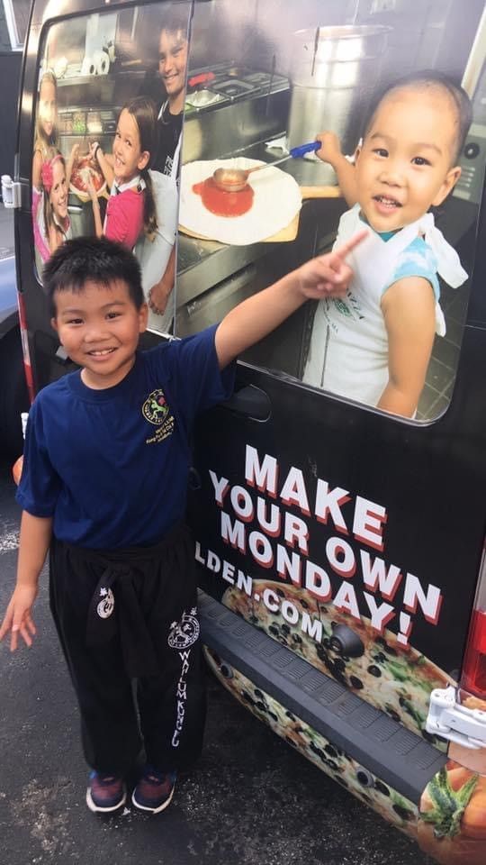 A young boy is standing in front of a van that says make your own monday.