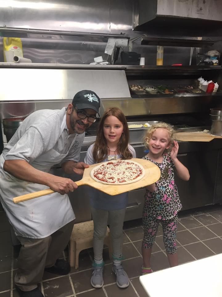 A man is holding a pizza paddle next to two girls.