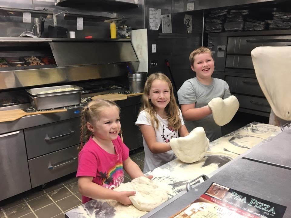 Three children are making pizza in a kitchen.