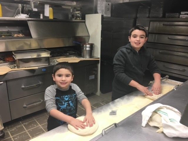 Two young boys are kneading dough in a kitchen