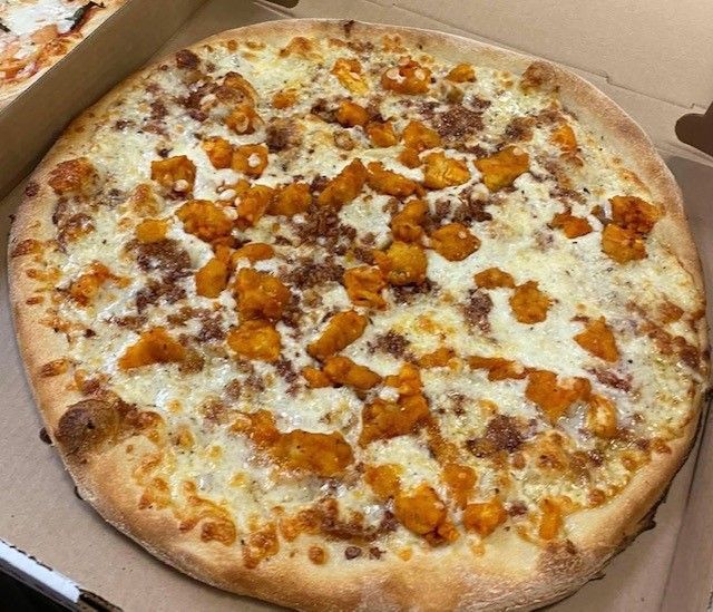A pizza with chicken and bacon on it is in a box.