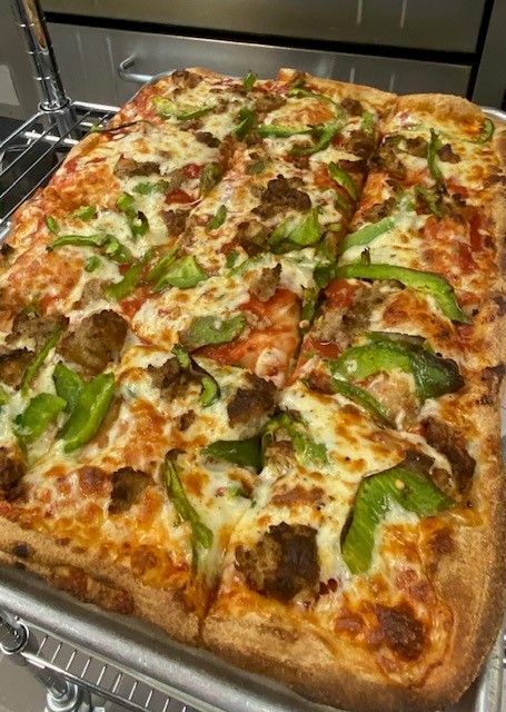 A pizza with pepperoni , sausage , tomatoes and cheese is sitting on a metal tray.