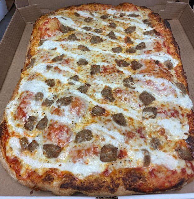 A large pizza with sausage and cheese is in a cardboard box.