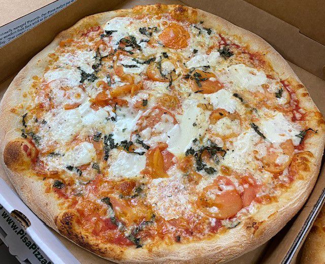 A pizza with tomatoes , cheese and basil is in a box.