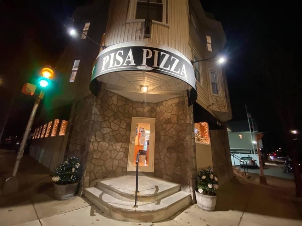 The entrance to pisa pizza is lit up at night.
