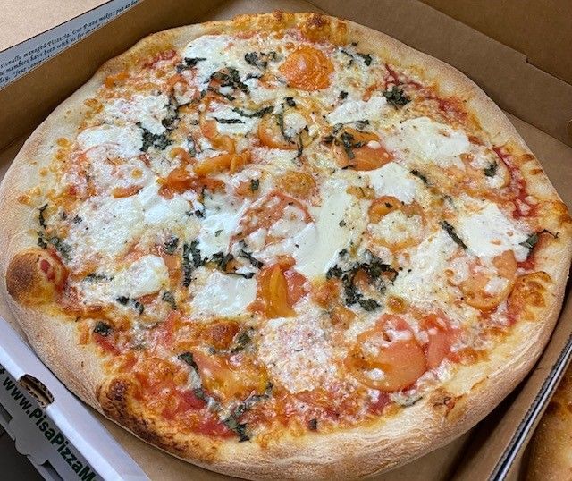 A pizza with tomatoes and cheese is in a cardboard box.