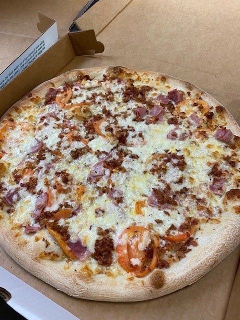 A pizza with bacon tomatoes and cheese in a box