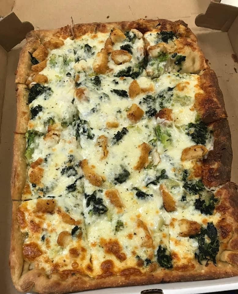 A pizza with spinach and chicken on it is in a box.