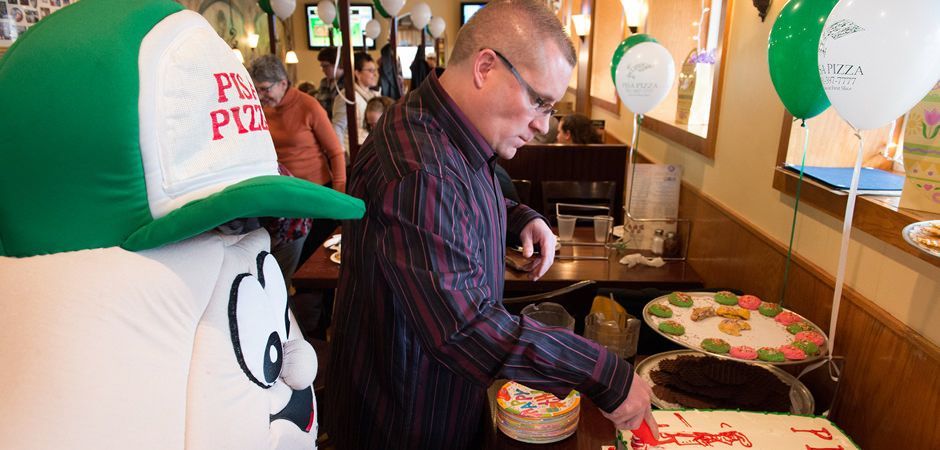 A man wearing a green hat is cutting a cake in a restaurant.