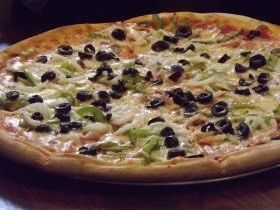 A pizza with olives , peppers , cheese and other toppings on a plate.