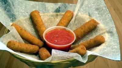 A basket filled with fried mozzarella sticks and a cup of dipping sauce.