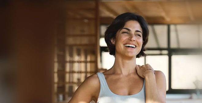 Woman in sports bra smiles, hand on hip, indoors.