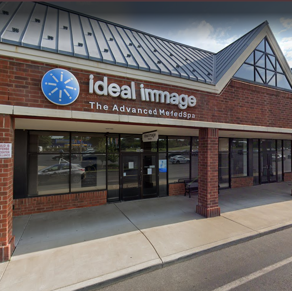 An Ideal Image MedSpa storefront with brick walls, large windows, and a metal roof in a shopping center.