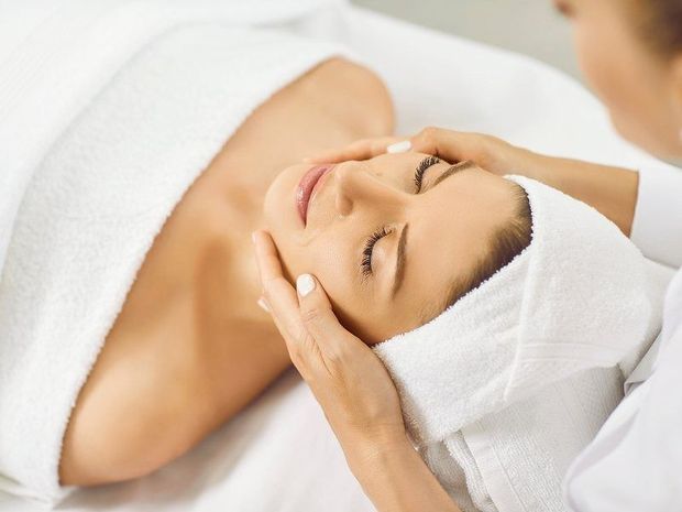 Woman receiving a facial massage while wrapped in a white towel and head wrap