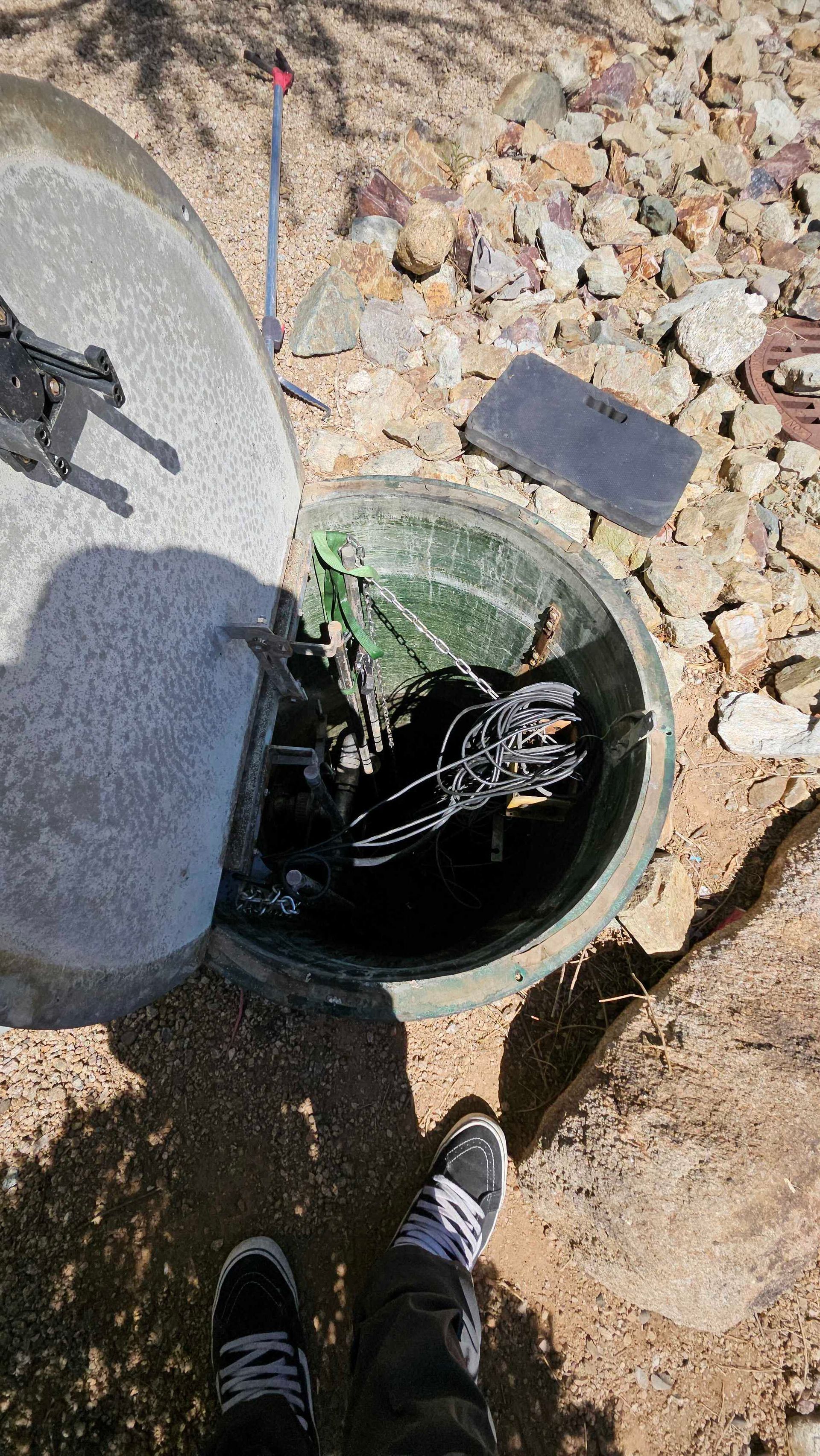 A person is standing next to a manhole cover with a cell phone in it.