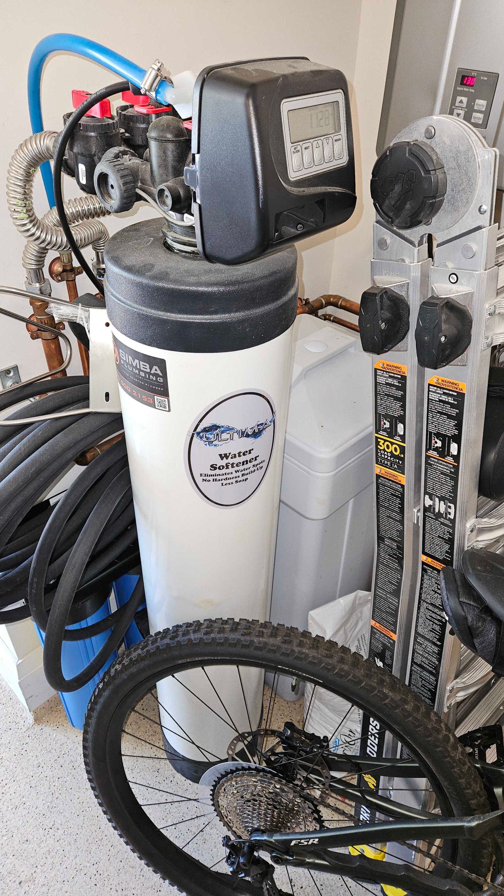 A bicycle is sitting next to a water softener in a garage.