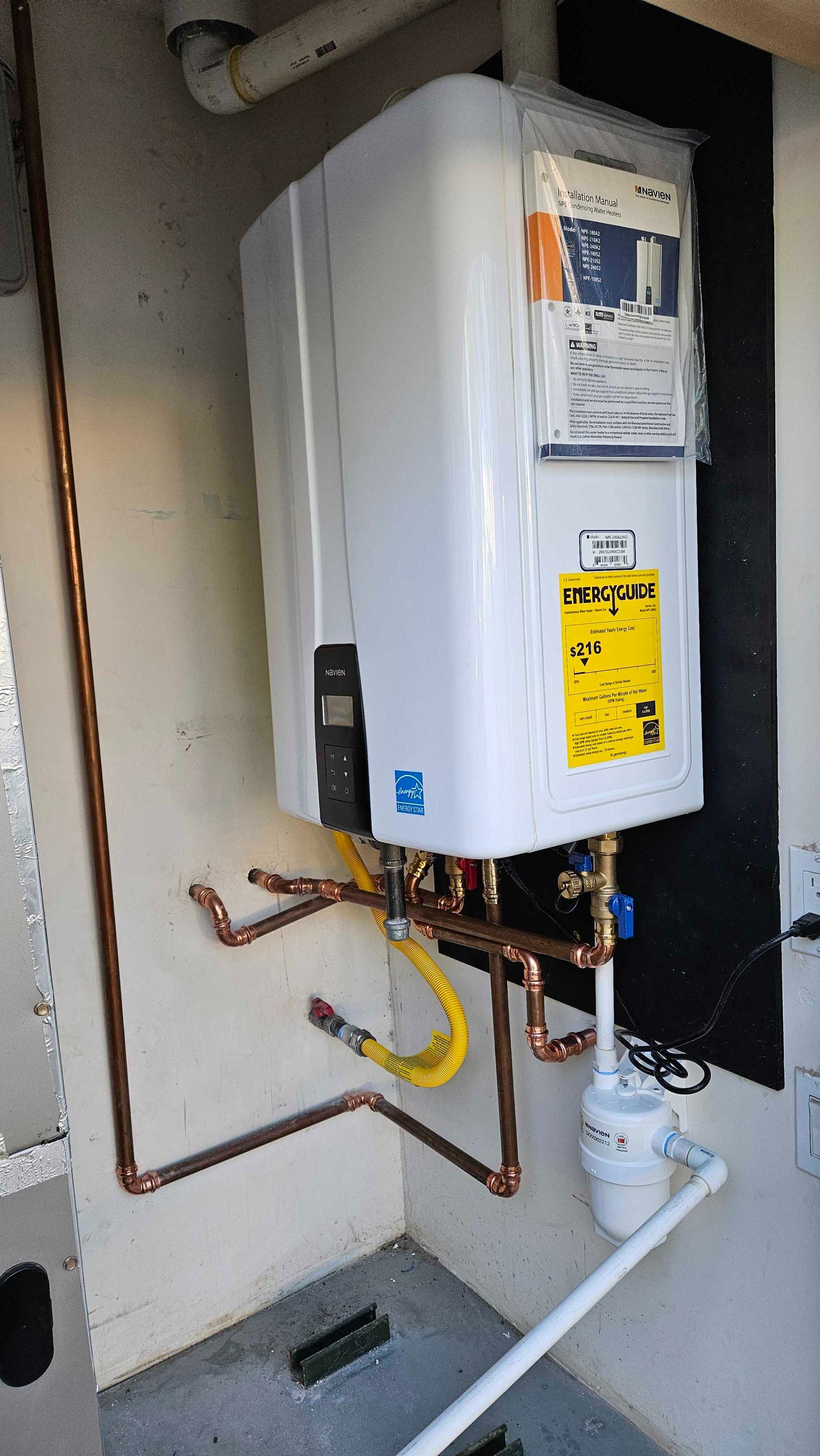 A white water heater is hanging on a wall next to copper pipes.
