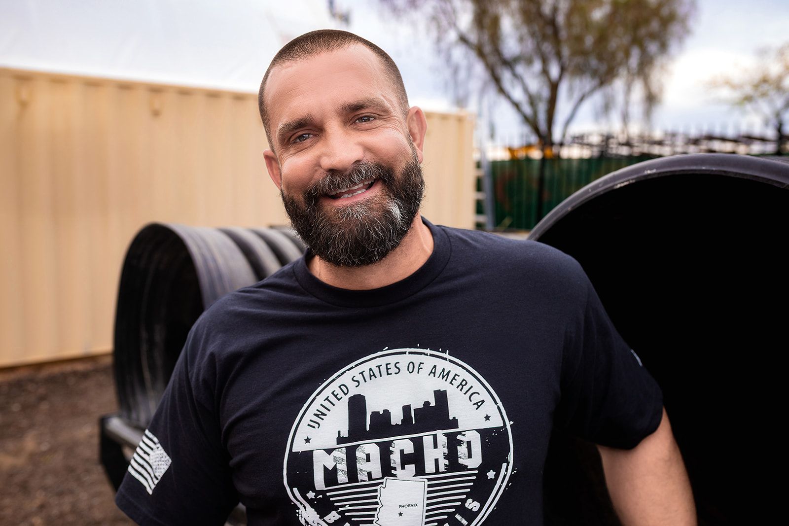 A man with a beard is wearing a black t-shirt with the word macho on it.