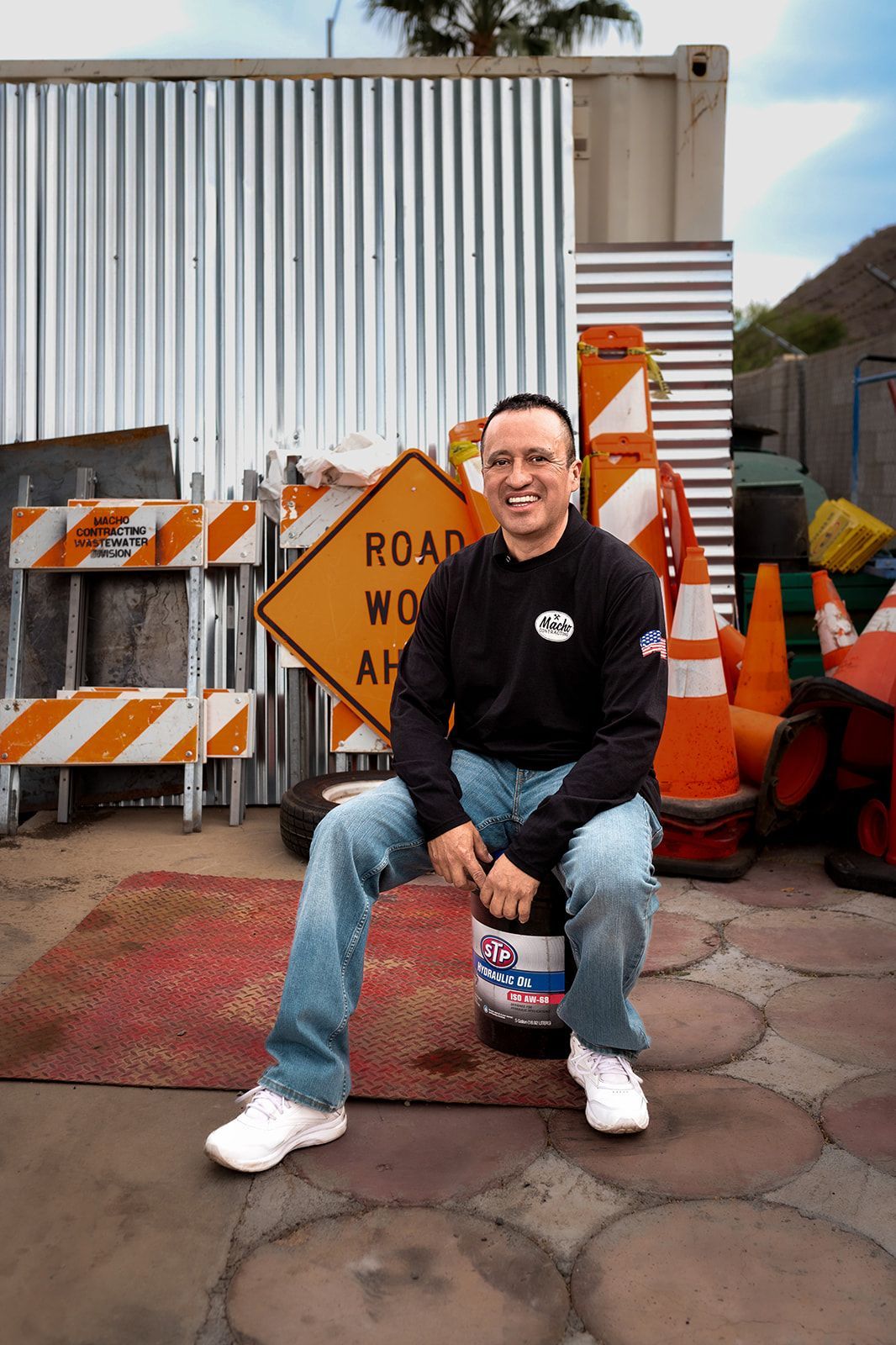 A man is sitting on a barrel in front of a sign that says road work ahead