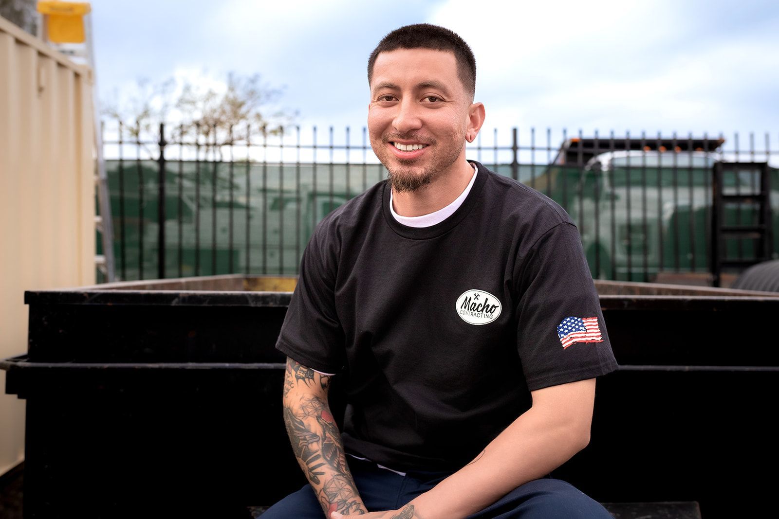A man with tattoos is sitting on the back of a truck.