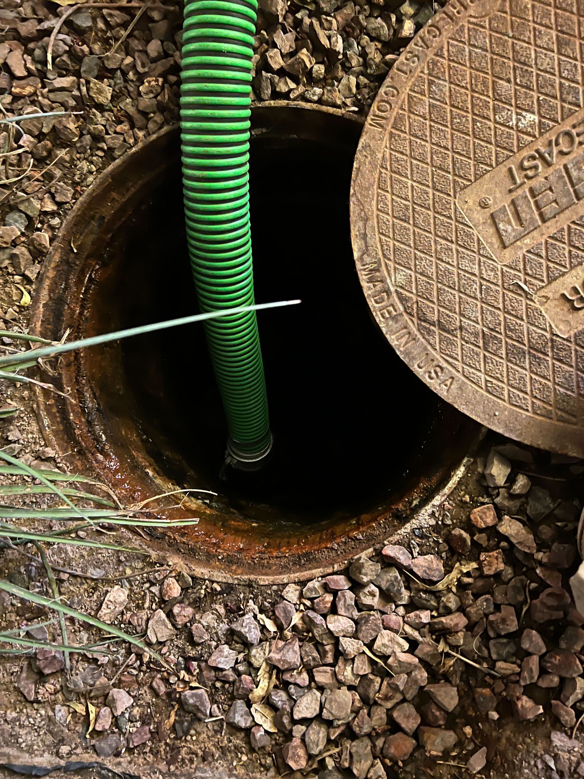 A green hose is coming out of a manhole cover.