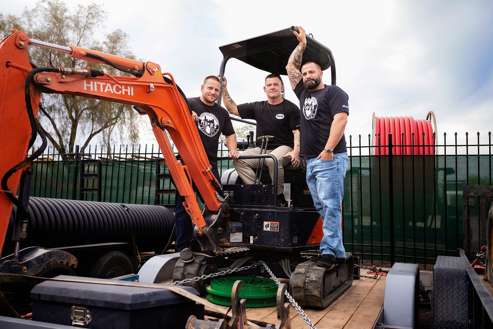 Three men are standing next to an excavator on a trailer.