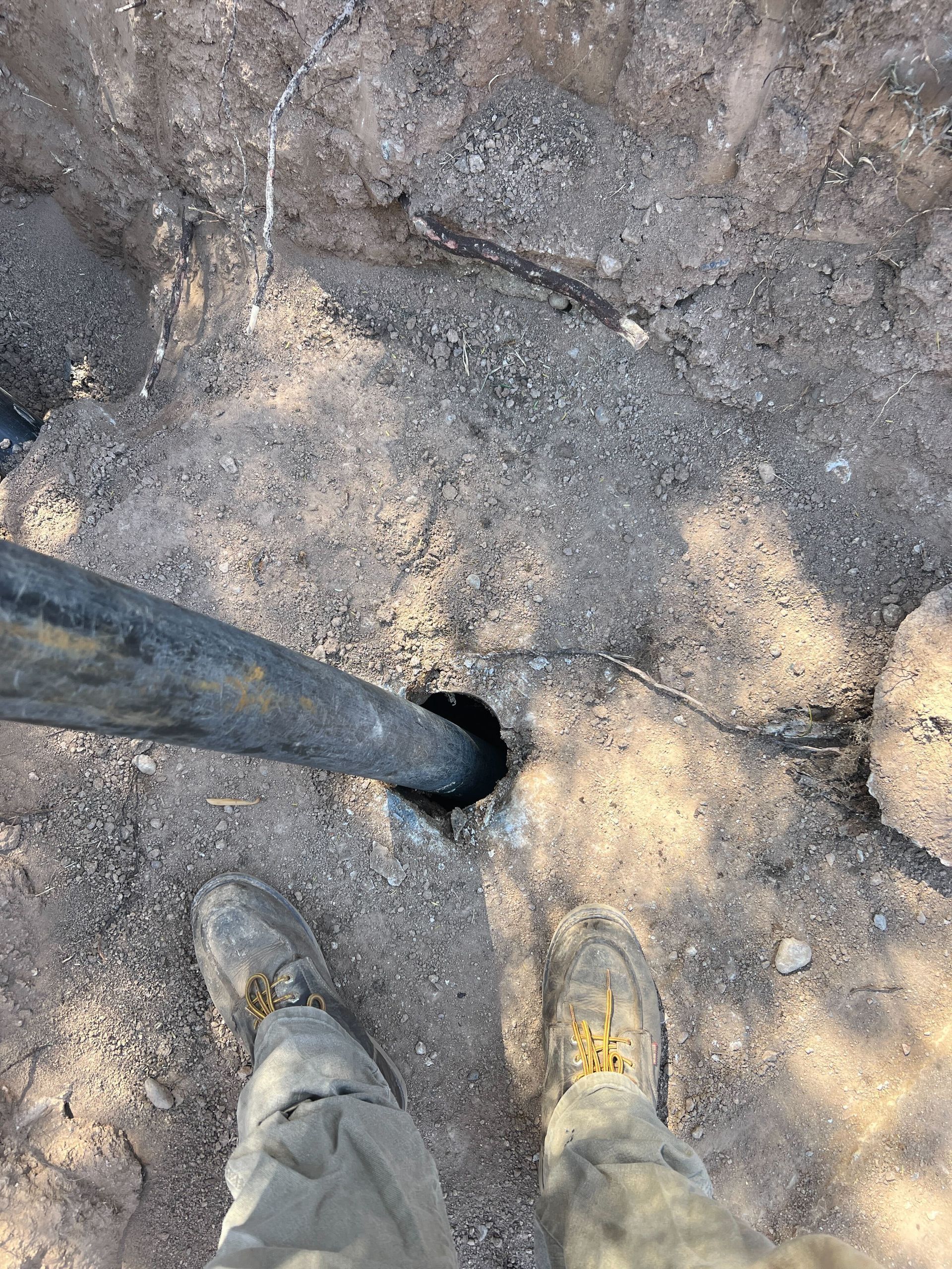 A person is standing next to a pipe in the dirt.