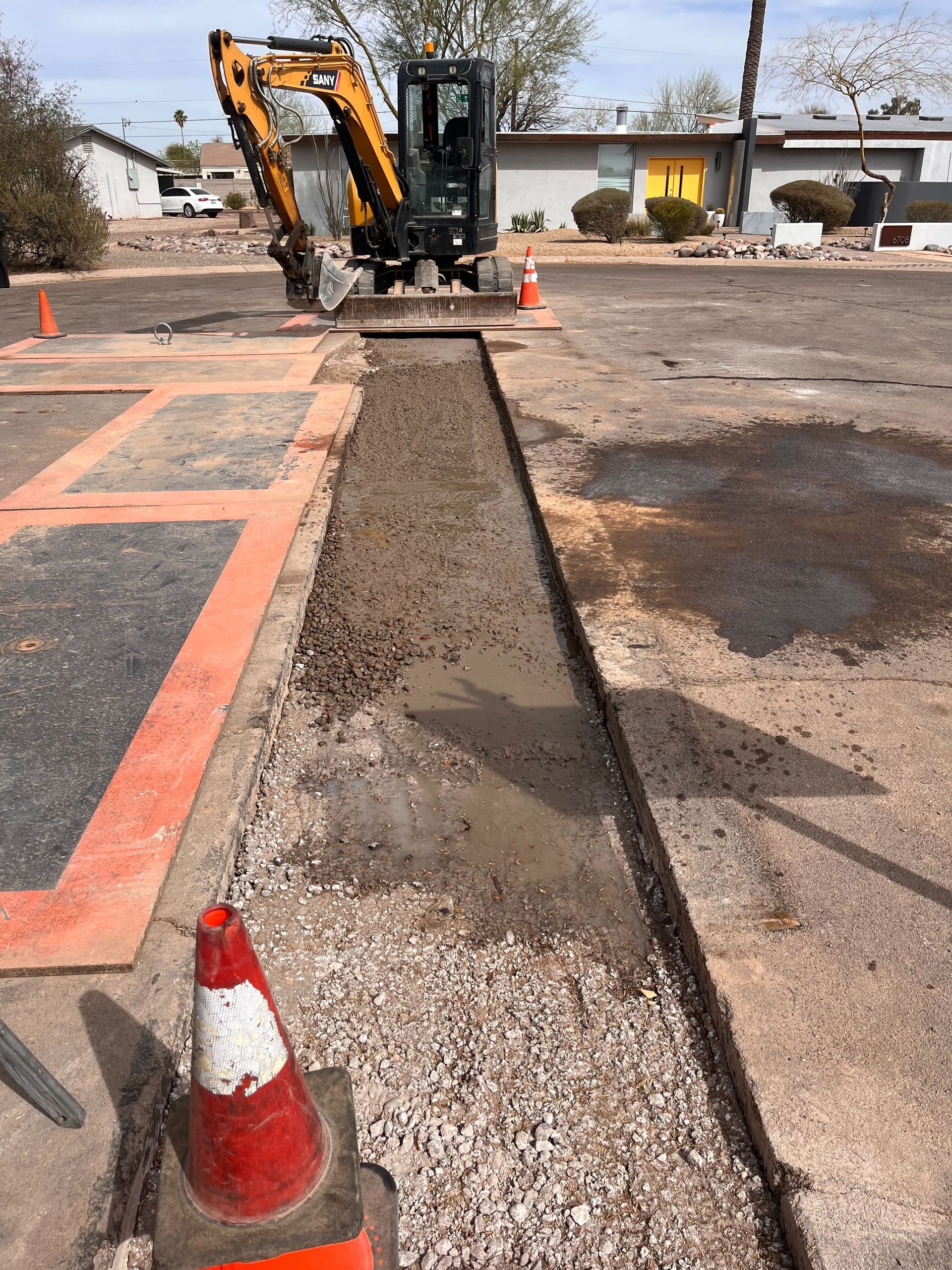 A construction vehicle is working on a sidewalk in a parking lot.