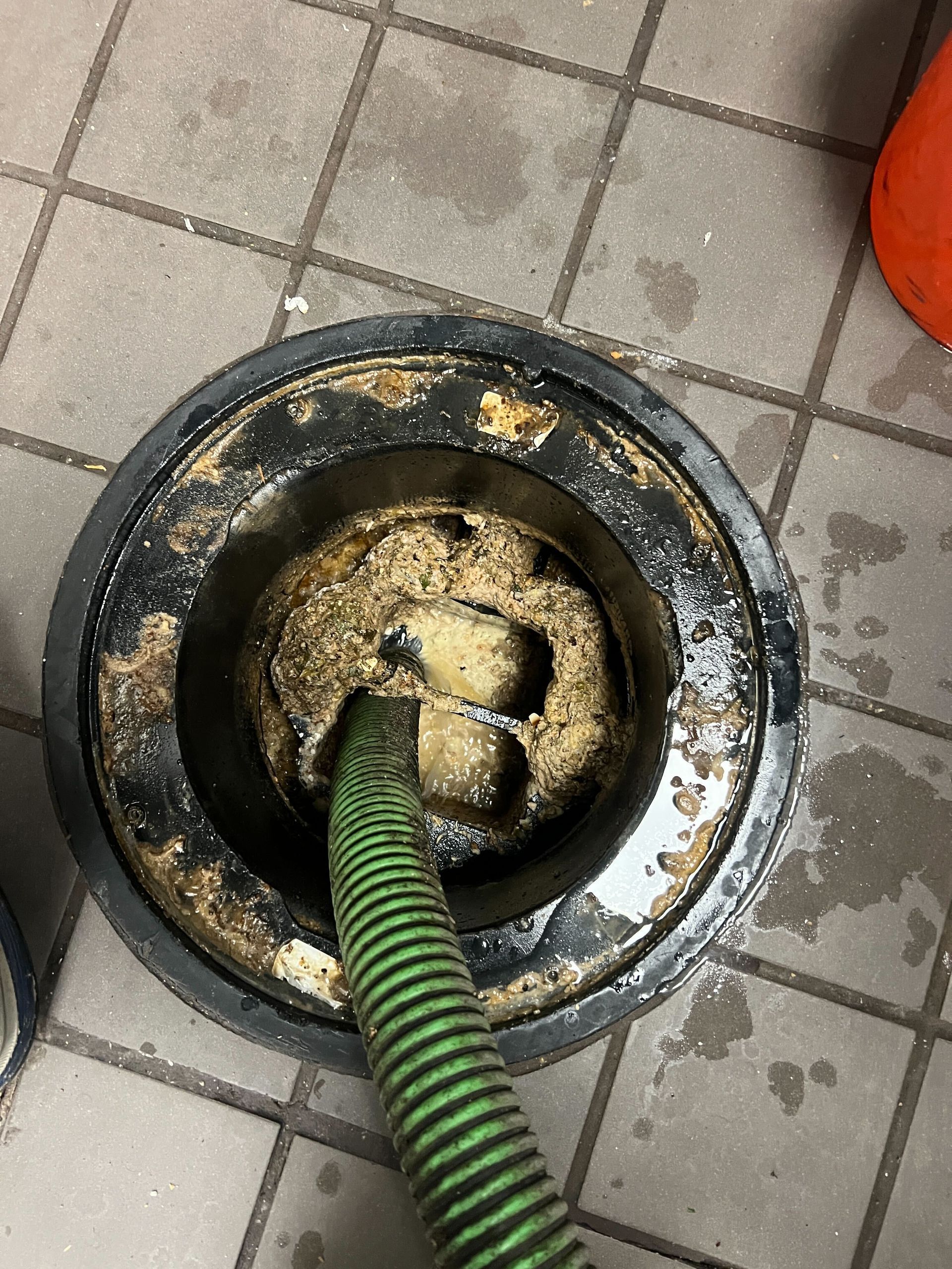 A green hose is being used to clean a drain on a tiled floor.