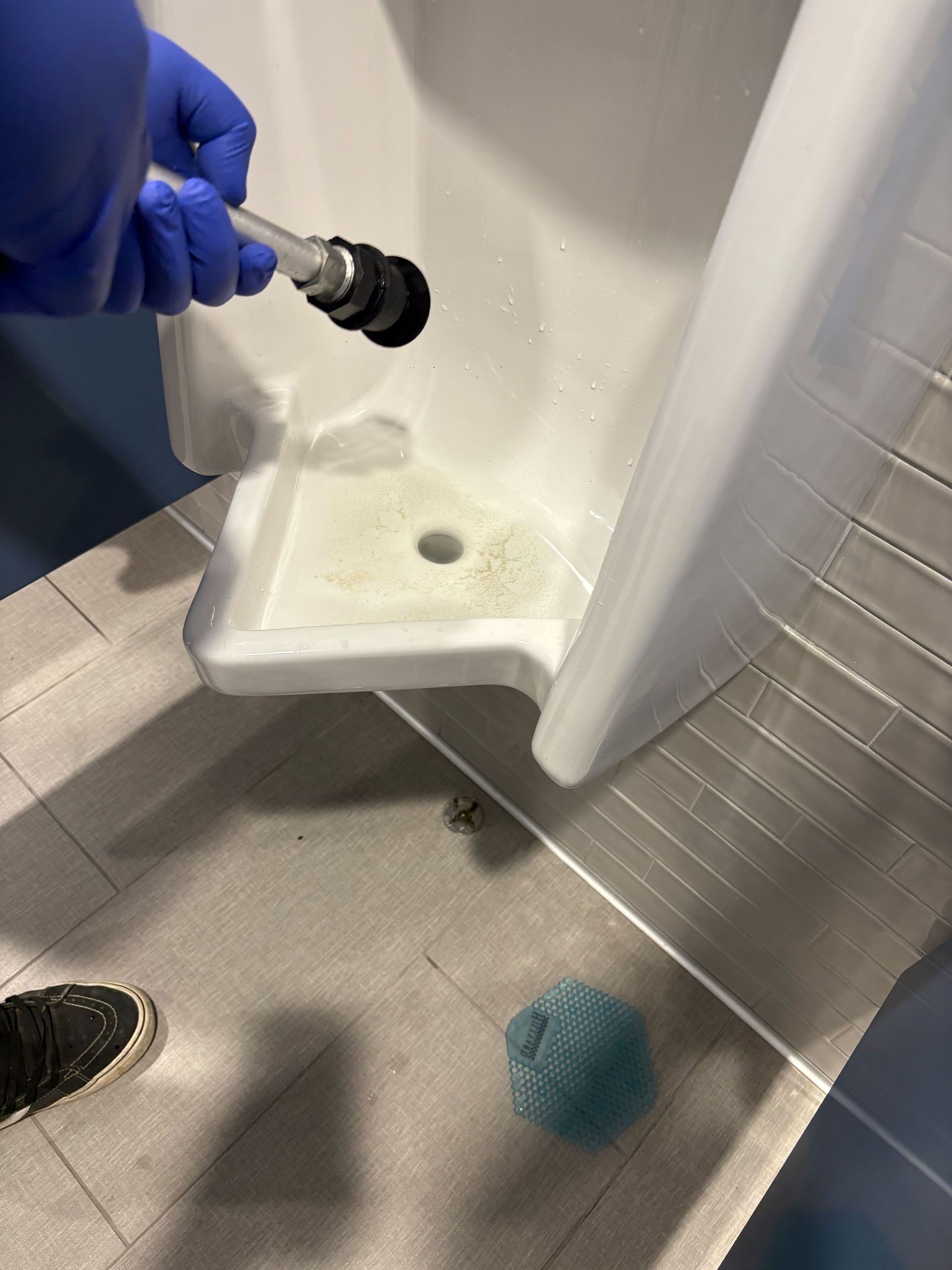 A person wearing blue gloves is cleaning a urinal with a spray bottle.
