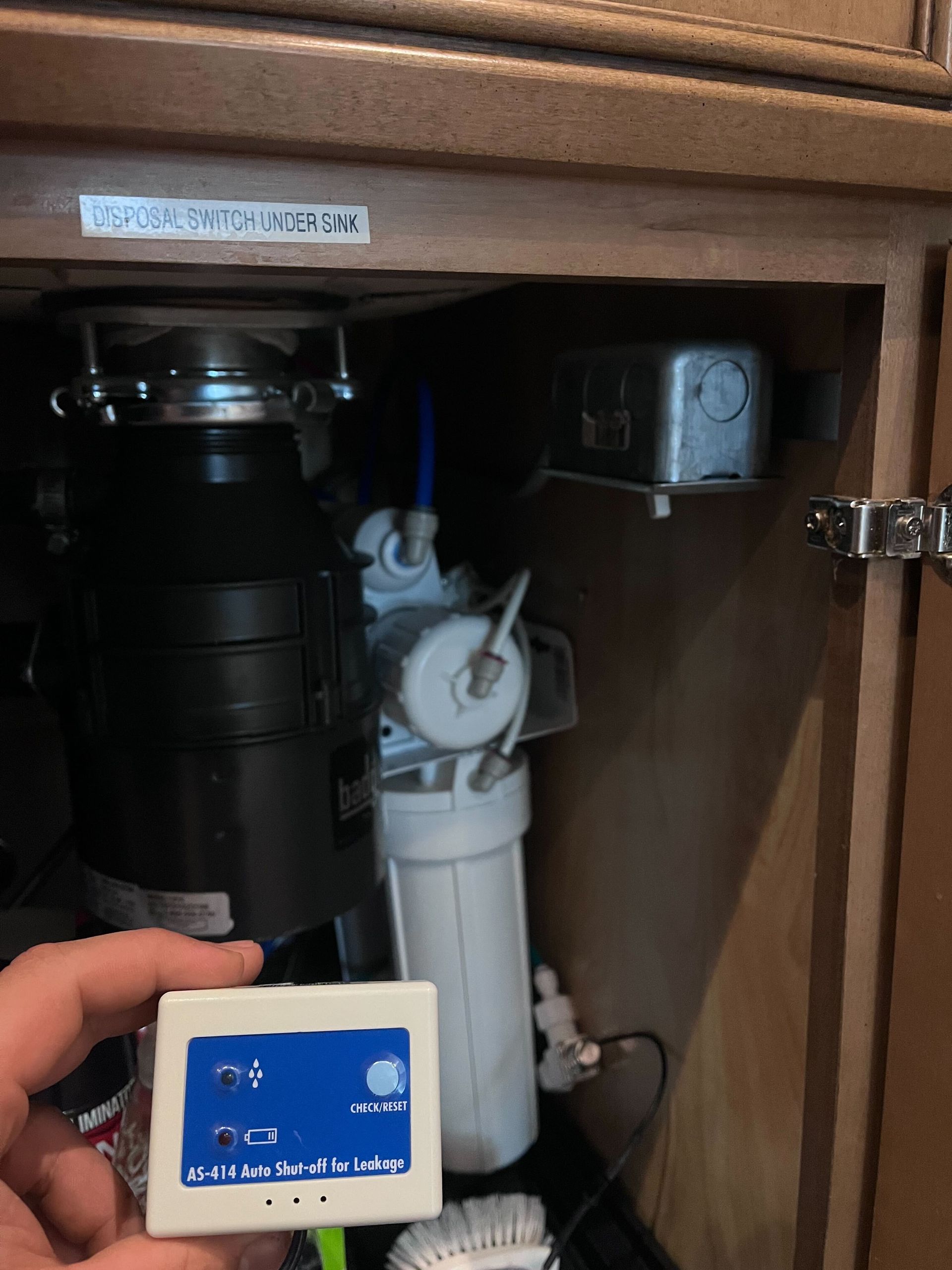 A person is holding a small device in front of a kitchen sink.