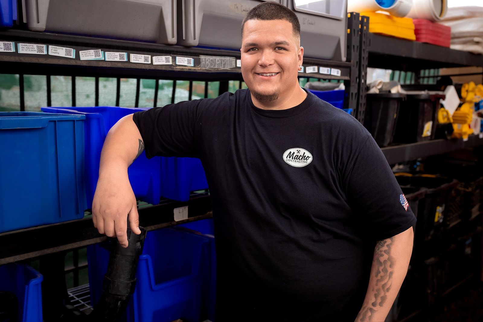 A man in a black shirt is standing in front of a shelf with blue bins.