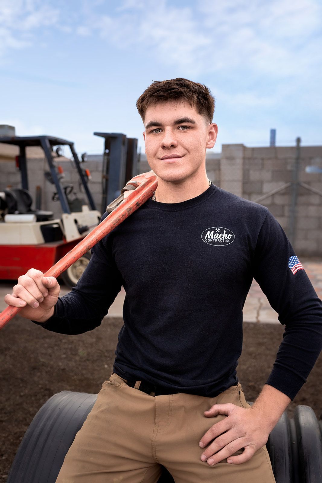 A young man is holding a hose over his shoulder in front of a forklift.