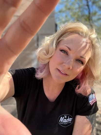 A woman wearing a black shirt with the word macho on it is taking a selfie.