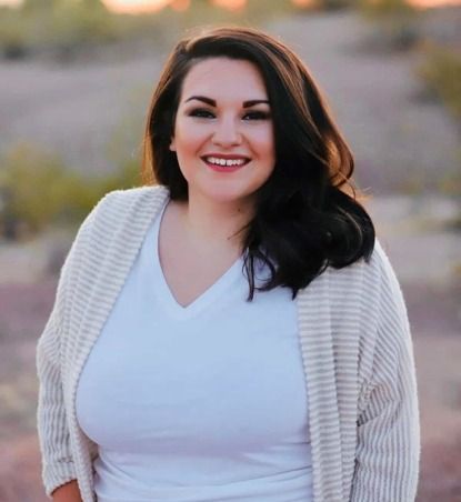 A woman wearing a white sweater and a white shirt is smiling for the camera.