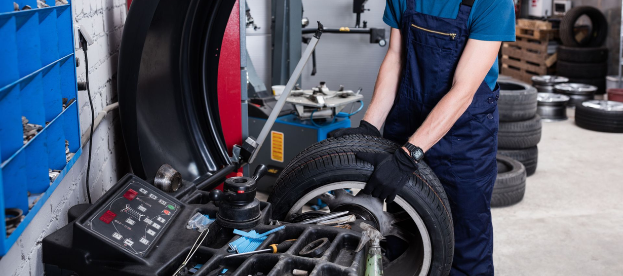 Mechanic in blue overalls balancing a tire on a machine.