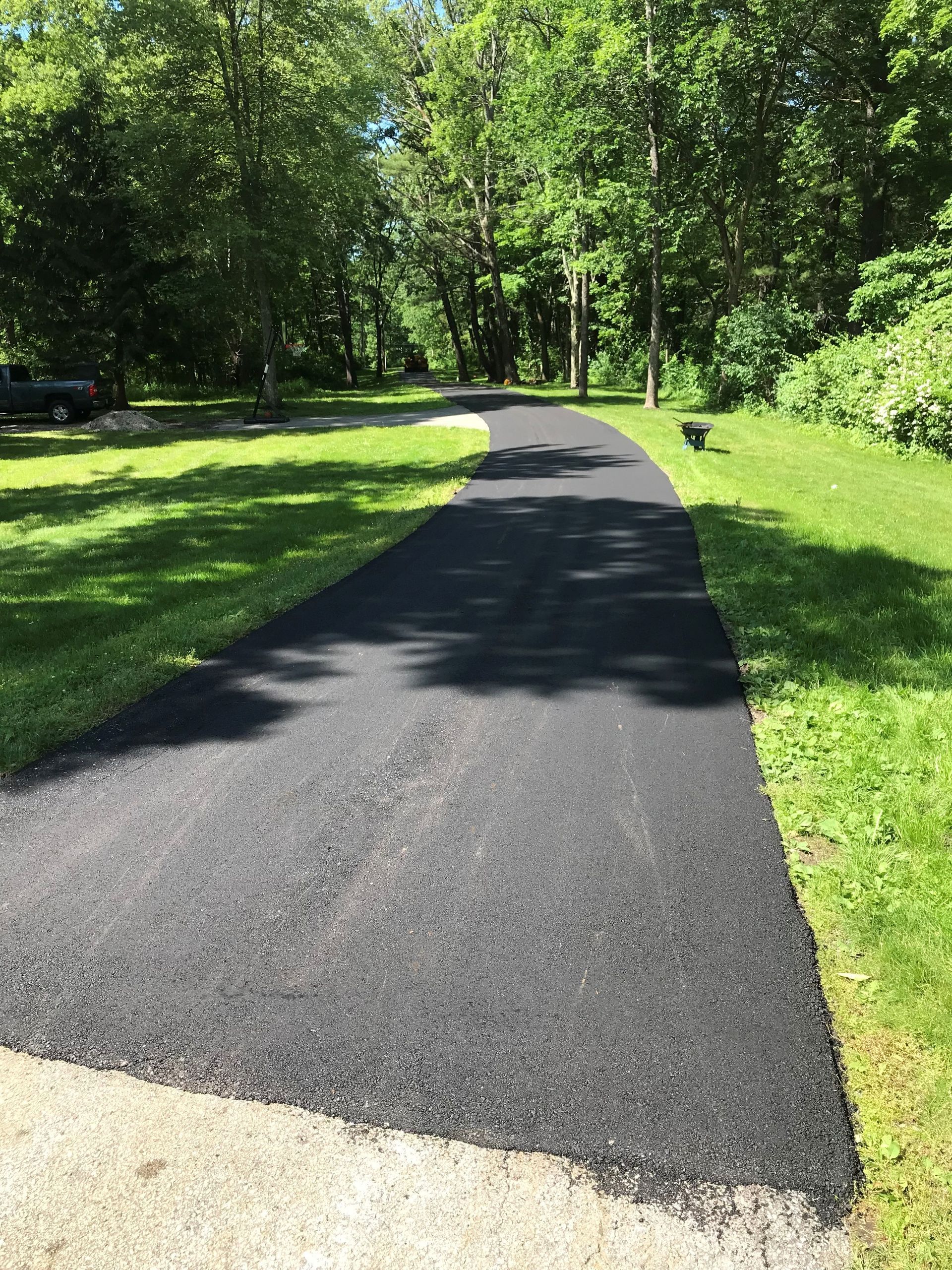 A black asphalt driveway going through a lush green field.