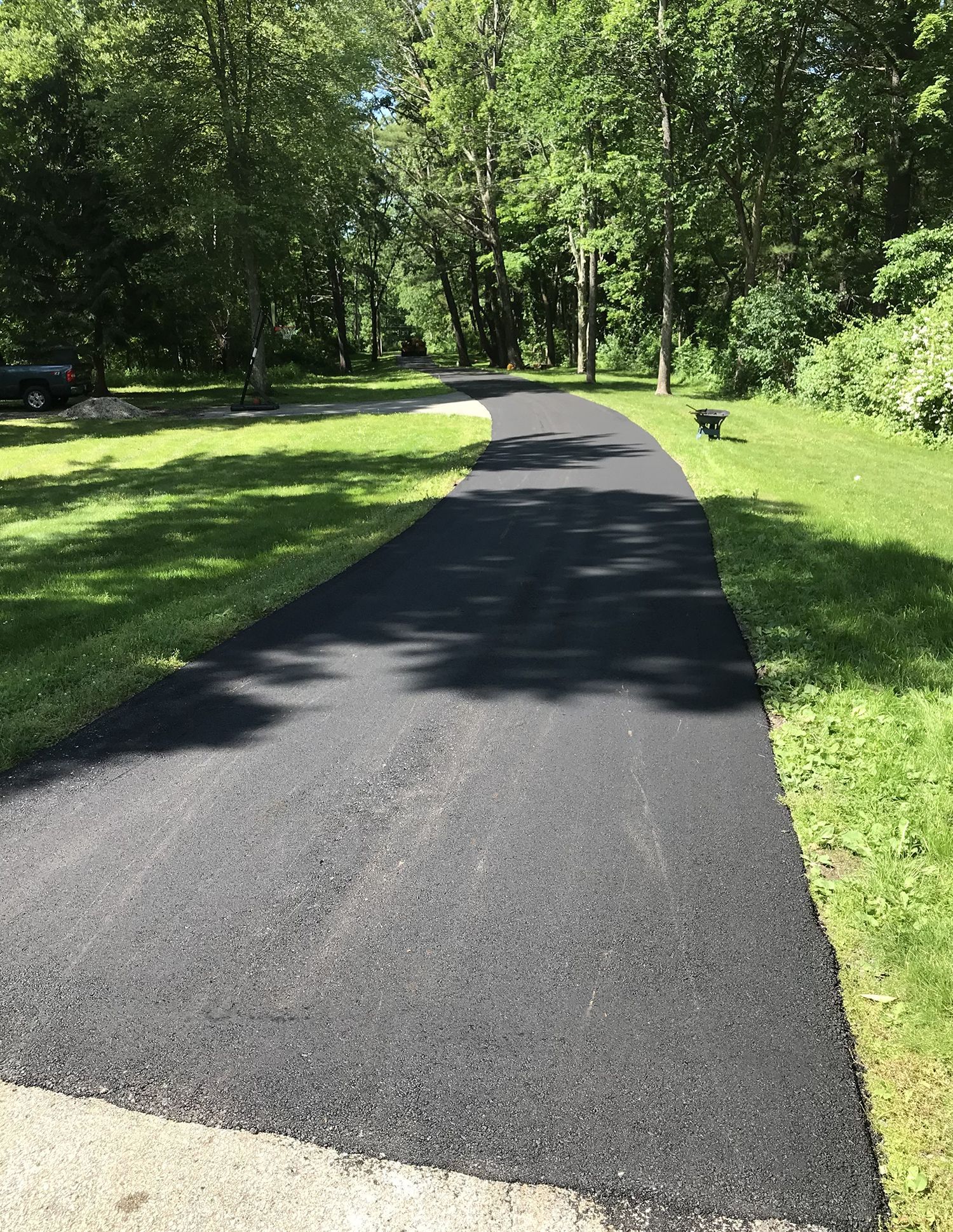 A black asphalt driveway going through a lush green field.