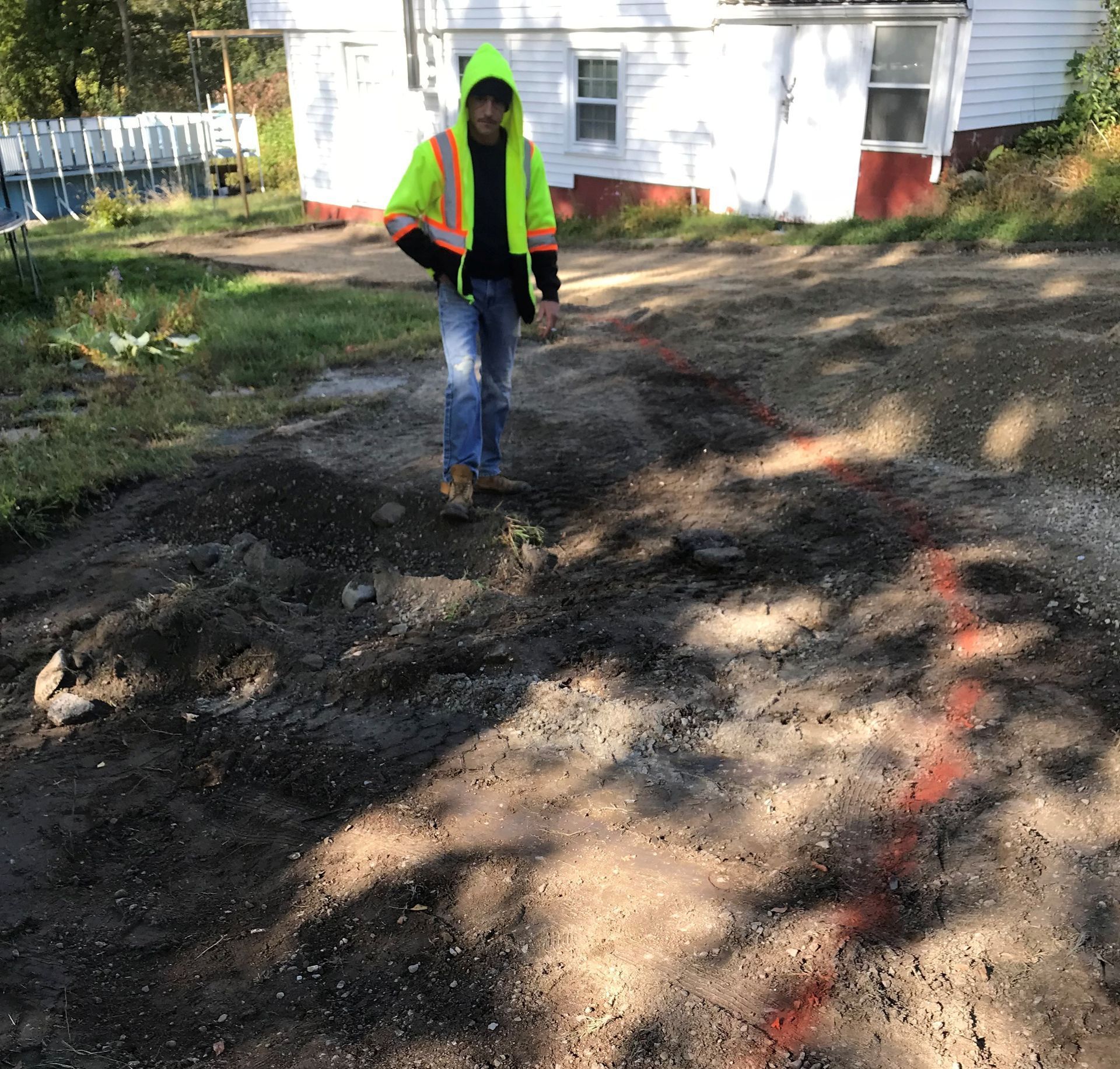 A man in a yellow vest is standing in the dirt in front of a house.