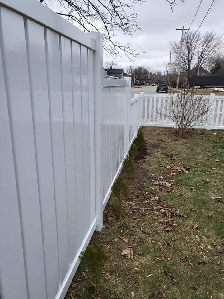 White vinyl fence bordering a grassy yard, with a picket section visible in the distance. Overcast sky.