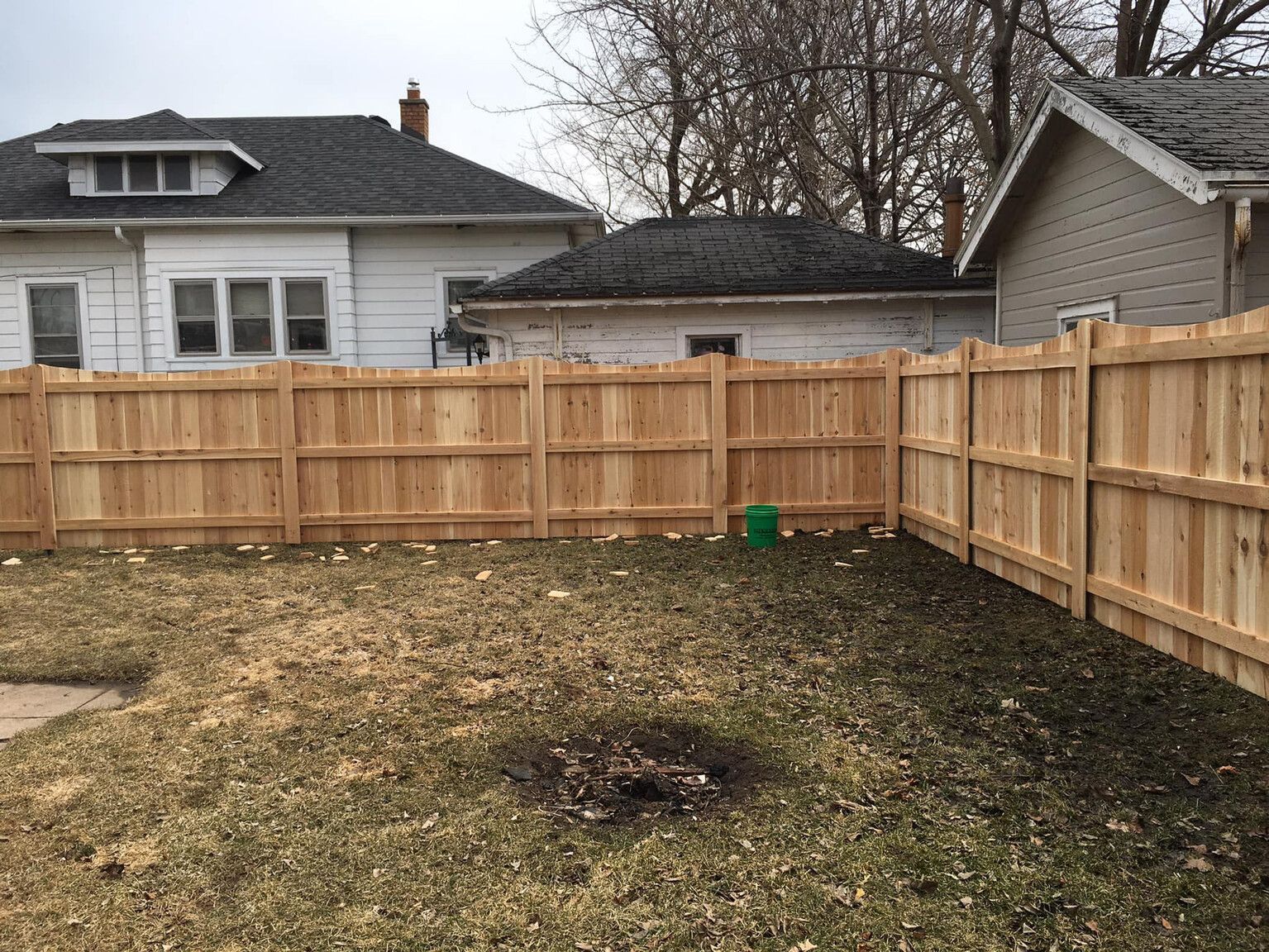 Wooden fence encloses a backyard with brown grass, in front of a house.