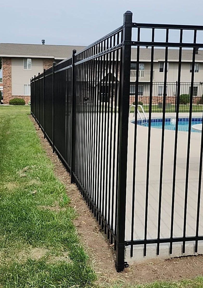 Black metal fence surrounding a pool next to a grassy area and apartment buildings.
