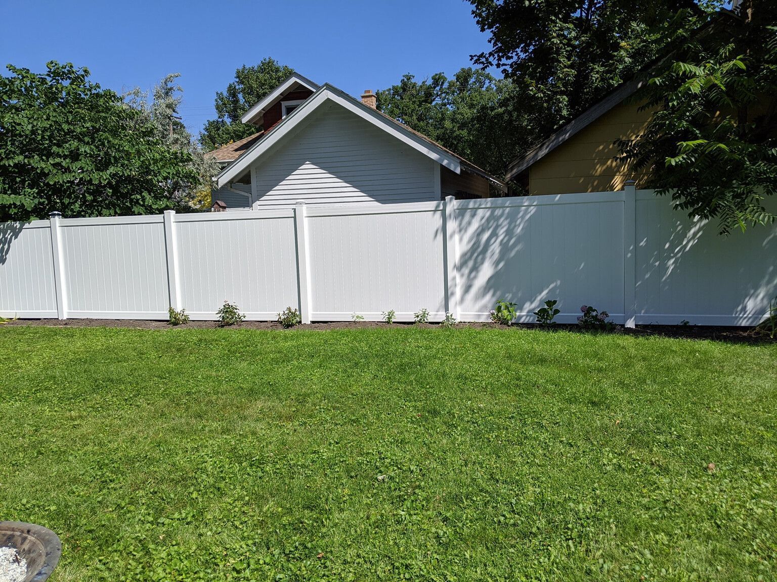 White vinyl fence in a grassy backyard, with a house visible behind it.