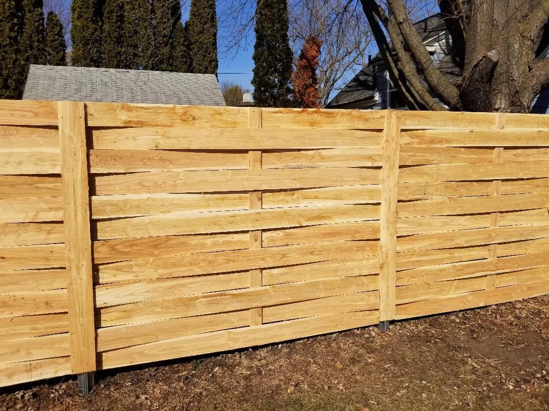 Wooden horizontal slat fence in a yard, trees in the background, daytime.