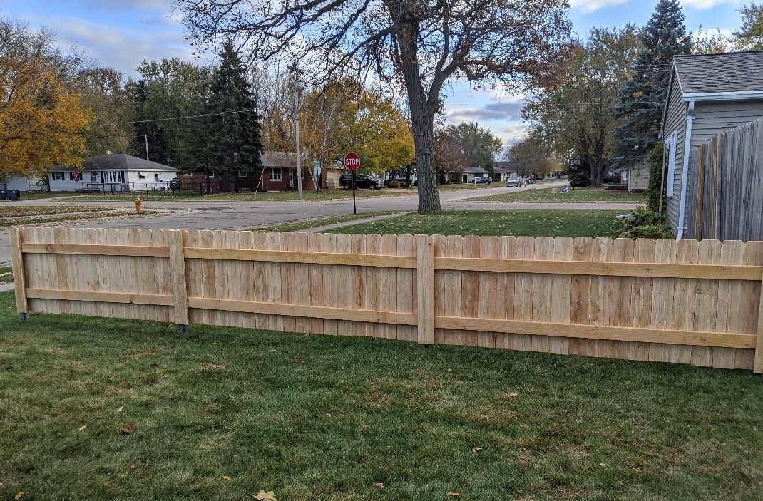 Wooden fence in front of a residential street with trees and houses. Overcast day.