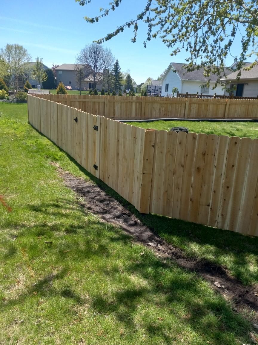 Wooden fence enclosing a grassy yard on a sunny day. Houses are visible in the background.