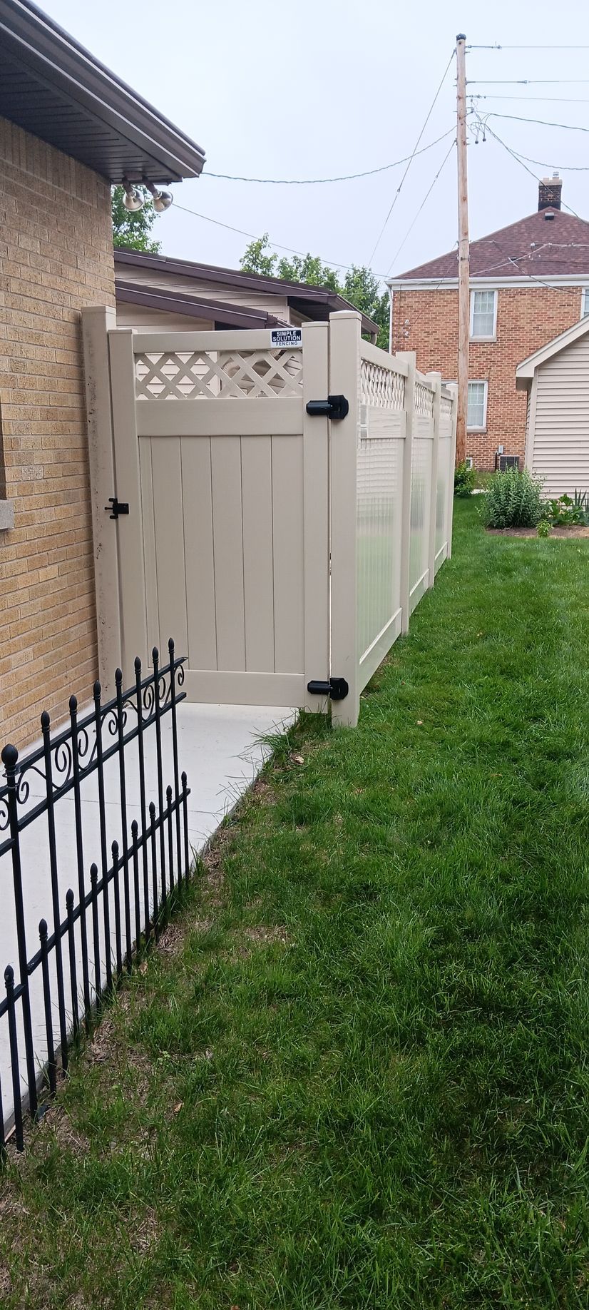 A beige vinyl fence separates a yard from a building. Green grass fills the yard.