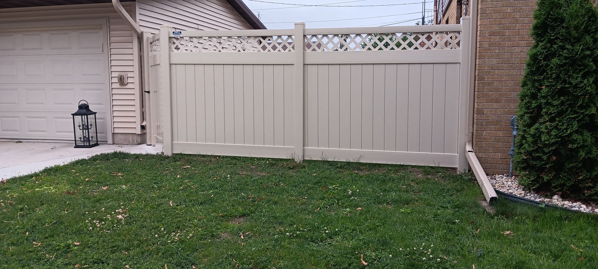 Beige fence with lattice top, green grass, and a garage in the background.